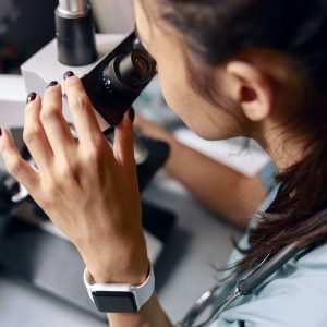 Scientist looks into microscope researching material sample at table in laboratory